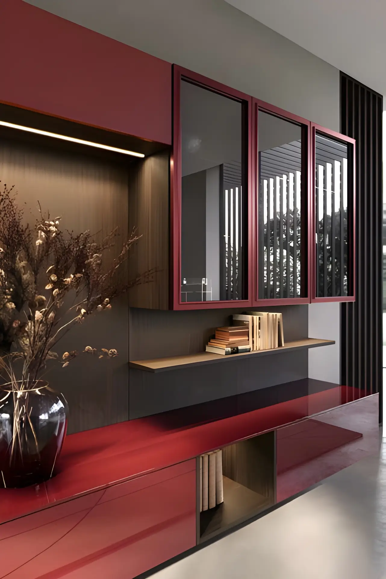 Aménagement intérieur moderne avec des armoires rouges, des miroirs muraux, une étagère en bois contenant des livres et un vase avec des fleurs séchées sur une surface rouge brillante.