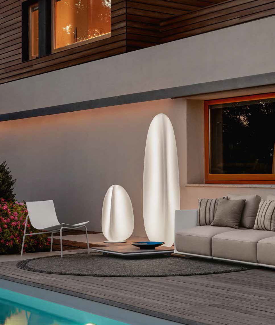 Un patio moderne avec une chaise blanche, un canapé beige, un tapis rond, une piscine et deux grandes lampes ovales lumineuses rehausse la décoration extérieure près d'un parterre de fleurs et de l'extérieur d'une maison en bois.