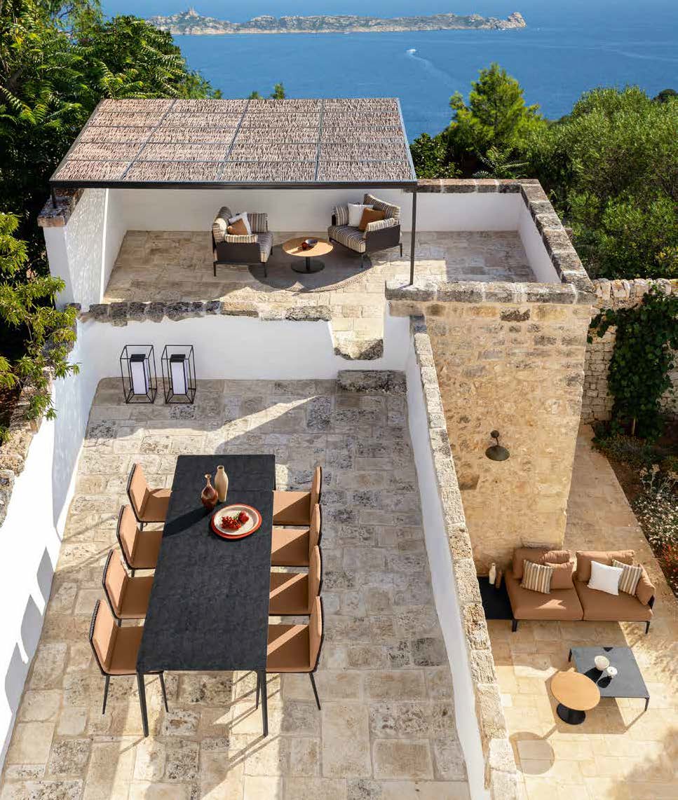 Patio en pierre avec table à manger et chaises au niveau inférieur, places assises au niveau supérieur, témoignant d'un aménagement extérieur bien pensé et offrant une vue imprenable sur la mer et une île au loin.