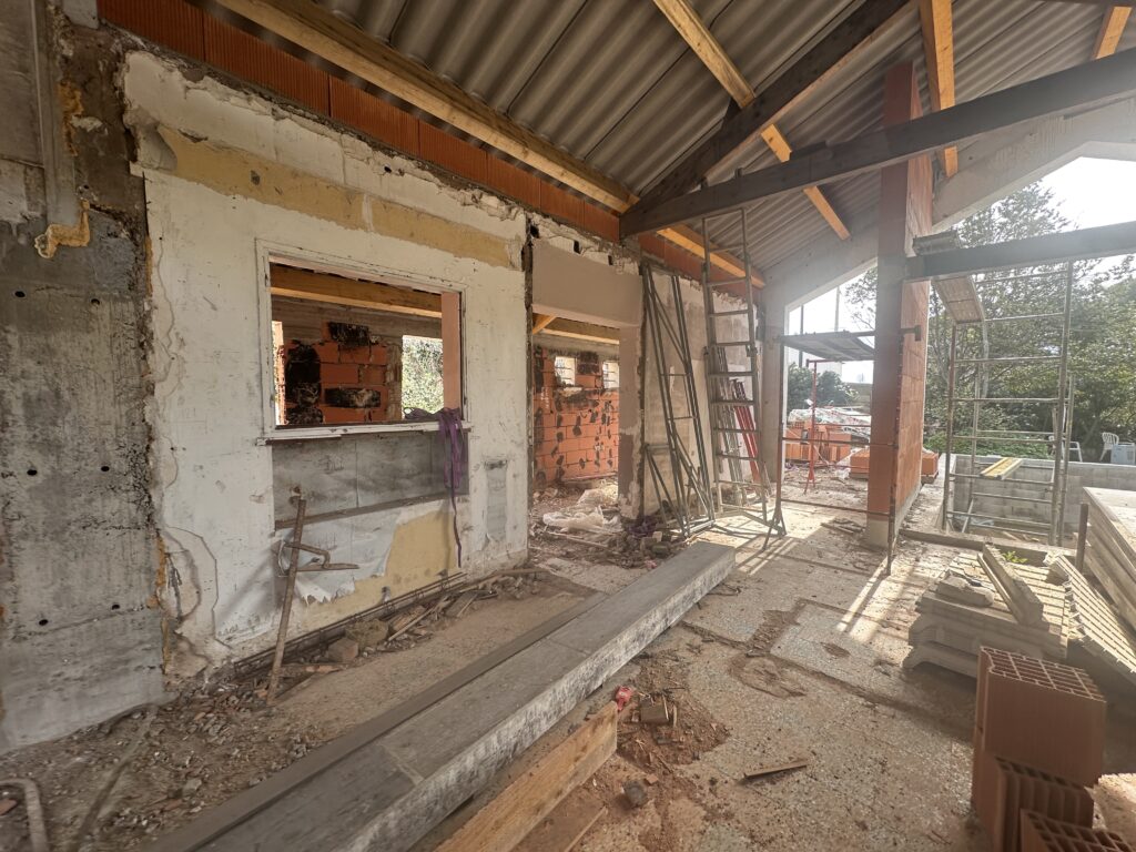 Intérieur d'un bâtiment partiellement démoli à Sète, illustrant l'aménagement intérieur, avec des murs apparents, des matériaux de construction, des échafaudages et la lumière du soleil qui traverse une structure de toit ouverte.